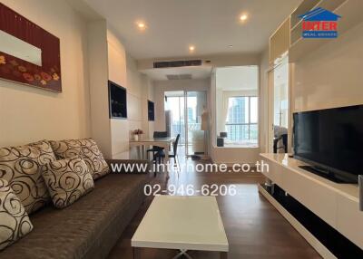 Modern living room with a sofa, coffee table, dining area, and large window with city view.