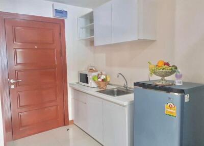 small kitchen with wooden door, white cabinets, microwave, sink, and a refrigerator