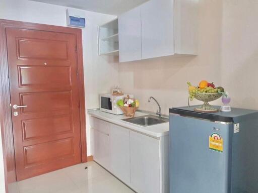 small kitchen with wooden door, white cabinets, microwave, sink, and a refrigerator