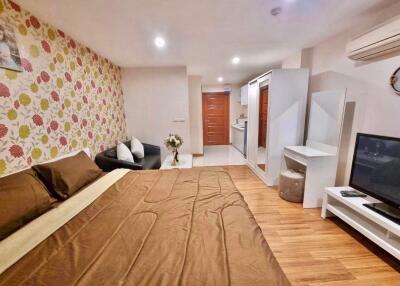 Modern bedroom with a double bed, decorative wallpaper, and an open view to a kitchenette.