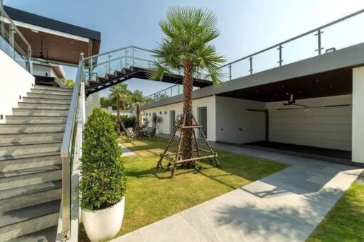 Modern outdoor area with stairs, glass railings, greenery, and a garage