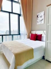 Modern bedroom with large windows, decorated with beige curtains, a white bed with red and beige pillows, and a wardrobe