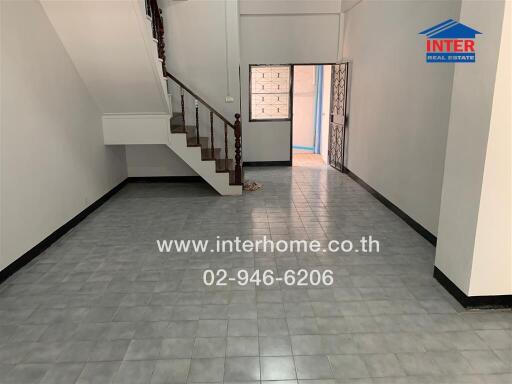 Spacious living room with tile flooring, stairs leading to the upper floor, and an open entryway.