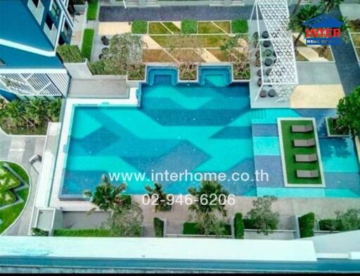Aerial view of a spacious outdoor swimming pool area with surrounding greenery and lounging area.