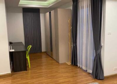 Modern bedroom with wood flooring, a desk, wardrobe, and large windows with curtains.
