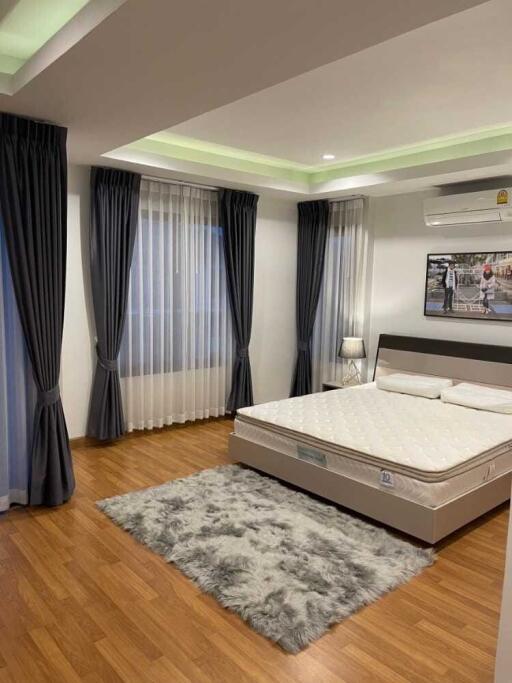 Modern bedroom with wooden floor, large windows with curtains, bed, and decorative rug