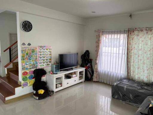 Living room with TV, stairs, and a window with floral curtains