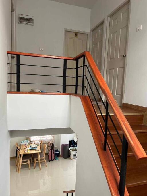 Interior view of a building showing a staircase with wooden handrails, doors on the upper floor, and a dining area on the lower floor