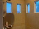 A modern bathroom shower with tan tiles and three small windows.