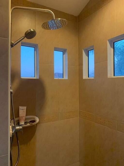 A modern bathroom shower with tan tiles and three small windows.