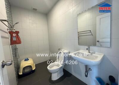 Modern bathroom with white tiled walls, a sink, toilet, and cat litter box