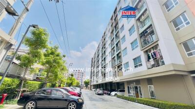 Outdoor view of a multi-storey residential building with parked cars and greenery