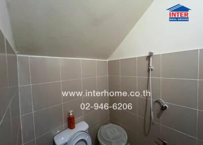 Small bathroom with beige tiles, a showerhead, and a toilet