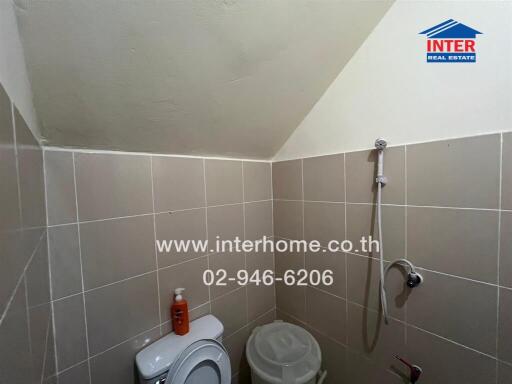 Small bathroom with beige tiles, a showerhead, and a toilet