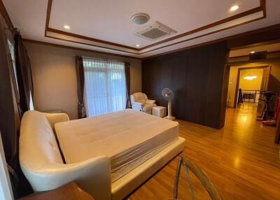 spacious bedroom with large window, bed, armchair, wooden flooring, and ceiling air conditioning