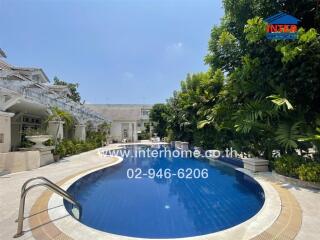 A pristine swimming pool with surrounding lush greenery and a view of the adjacent building