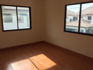 Empty bedroom with two windows and wooden flooring.