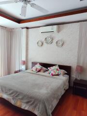 Modern bedroom with large bed, ceiling fan, air conditioner, bedside tables, and decorative wall pieces