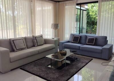 Well-lit modern living room with large windows, two couches, coffee table, and a ceiling fan