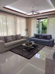 Well-lit modern living room with large windows, two couches, coffee table, and a ceiling fan