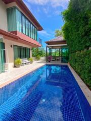 Outdoor pool area next to a modern house with green surroundings