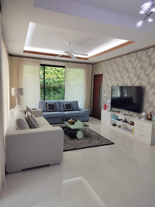 Bright and modern living room with large windows, white sofa set, and TV.