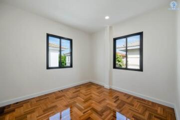 Empty bedroom with wooden parquet floor and two windows.