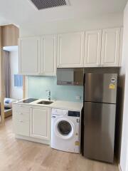 Compact modern kitchen with white cabinets, washing machine, and stainless steel refrigerator