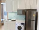Compact modern kitchen with white cabinets, washing machine, and stainless steel refrigerator