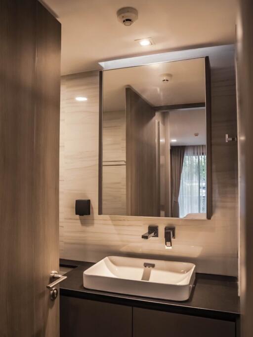 Modern bathroom with wooden door, rectangular sink, large mirror, and overhead lighting
