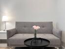 Modern living room with a grey sofa, side table with lamp, black coffee table with a vase of flowers