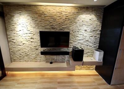 Modern living room with a stone accent wall, mounted TV, floating shelves, and under-cabinet lighting