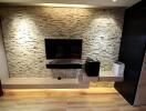 Modern living room with a stone accent wall, mounted TV, floating shelves, and under-cabinet lighting