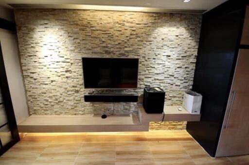 Modern living room with a stone accent wall, mounted TV, floating shelves, and under-cabinet lighting