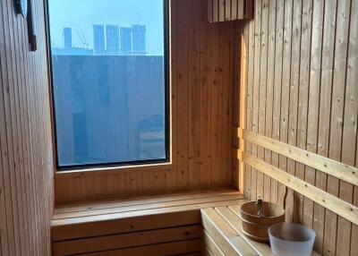 A well-lit sauna with wooden walls and benches, featuring a view of the city.