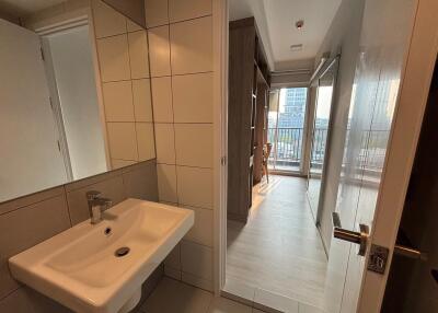 View of a bathroom sink adjacent to a hallway leading to a room with a seating area and balcony access