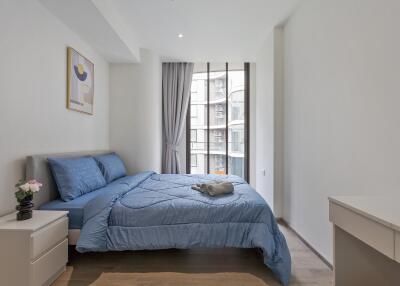 A modern bedroom with a large window and blue bed linens