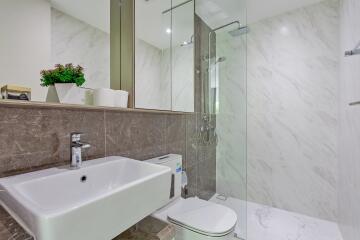 Modern bathroom with a glass-enclosed shower, sink, toilet, and marble tiles