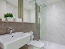 Modern bathroom with a glass-enclosed shower, sink, toilet, and marble tiles
