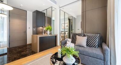 Modern living room with gray sofa, decorative cushions, coffee table with plants, and view of kitchen