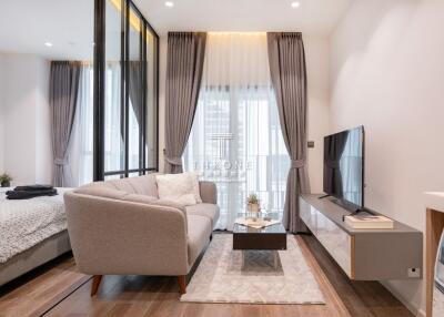 Modern living room with a large window, sofa, flat-screen TV, and access to a bedroom