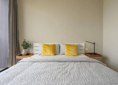 Modern bedroom with a neatly made bed, yellow accent pillows, bedside tables and a lamp