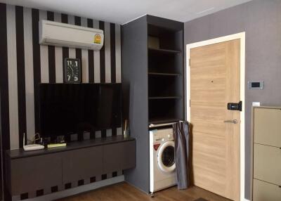 Modern living area with TV, air conditioner, washing machine, and wooden flooring