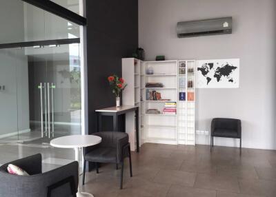 Modern living area with bookshelf, chairs, air conditioning, and glass doors.