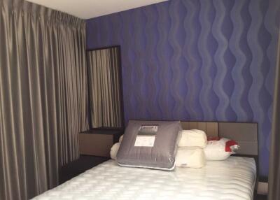 Bedroom with blue patterned wall, a bed with multiple pillows, sheer grey curtains, and a mirror