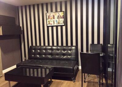 Living room with modern decor featuring black leather sofa, glass coffee table, striped wallpaper, and a painting.