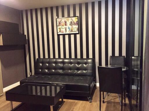 Living room with modern decor featuring black leather sofa, glass coffee table, striped wallpaper, and a painting.