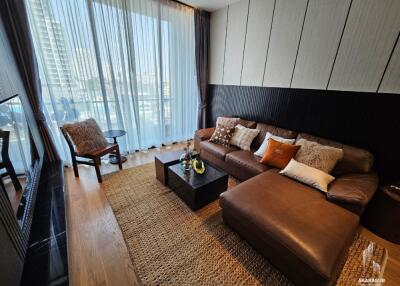 Modern living room with comfortable brown sofa, large windows with sheer curtains, and city view