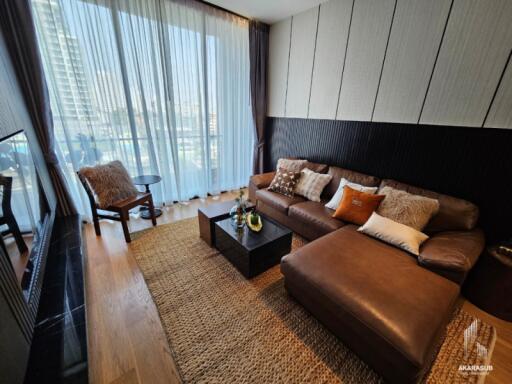 Modern living room with comfortable brown sofa, large windows with sheer curtains, and city view