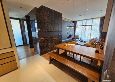 Modern dining area with wooden table and benches, adjacent to a cozy living space.